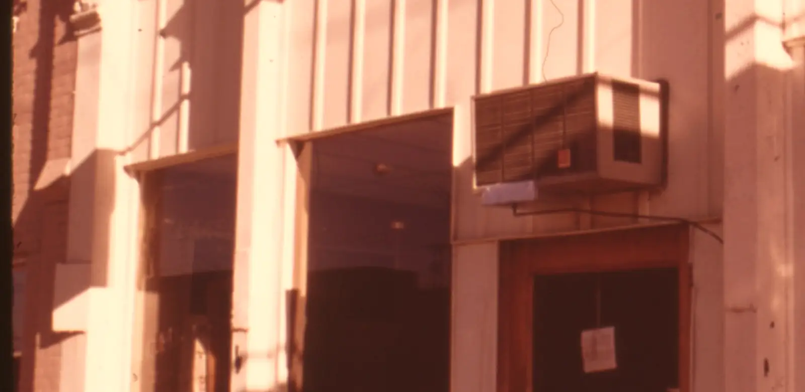Archival photograph of another small-town bakery: its storefront in late-afternoon light, plate glass, a wooden door and painted columns.